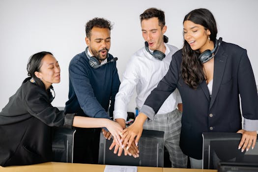 A diverse group of colleagues in an office setting putting their hands together to symbolize teamwork.