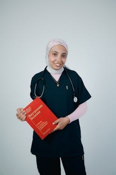 Doctor in scrubs with stethoscope holding a medical book, studio shot.