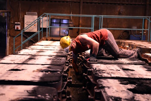 Worker inspecting machinery in an industrial plant wearing safety gear.